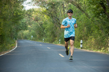 The young man runs on the black road in the middle of nature.
