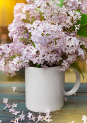 A white Cup with lilac on a vintage wooden surface on spring raining day. 