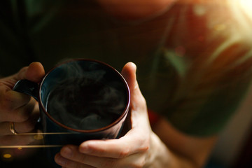 A dark large mug with a hot drink and steam from tea in men's hands. Close-up coffee mug, pleasure...