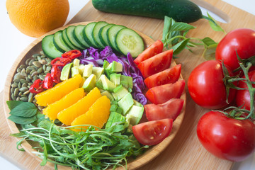 A buddha bowl of fresh summer healthy rainbow salad with cucumbers, tomatoes, arugula, basil, pumpkin seeds, avocado, red cabbage and chilli pepper on a wooden surface