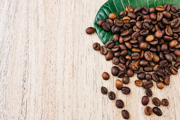 Coffee beans on a green leaf and scattered on a light wooden table, top view, closeup grains, flat lay, place for text, copy space