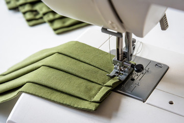Close-up view on a homemade reusable cloth face mask in green cotton fabric being sewn on a sewing machine.