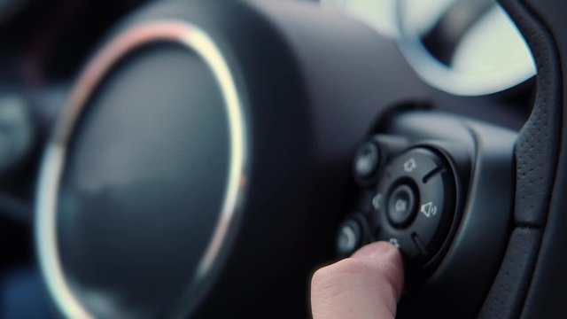 Close-up of the finger of a male driver who, with the help of shortcuts, steering wheel sound buttons, controls the increase and decrease of volume. Modern car with remote control audio system.