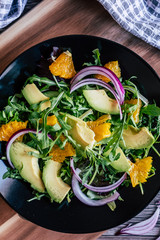 Salade verte avec des tranches d'avocat et d'orange  dans une assiette noire - Alimentation fraiche et saine