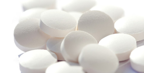 Heap of simple tiny round white pills loose, group of small tablets on white, macro, closeup, focus on one pill. New medicine, supplements and drugs bulk concept. Hi key shot, shallow depth of field