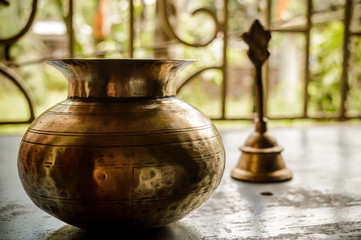 Fototapeta na wymiar Close up Still Life of antique Holi water pot and bell on rustic floor. Faith, Tradition, Spirituality, Prayer, symbols of peace and Religious Themes. Arts and culture background concept. Copy space