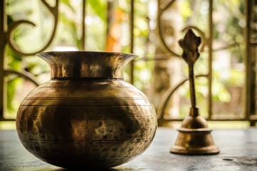 Close up Still Life of antique Holi water pot and bell on rustic floor. Faith, Tradition, Spirituality, Prayer, symbols of peace and Religious Themes. Arts and culture background concept. Copy space.