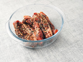 Pork belly slices marinated in soy sauce and herbs in a glass bowl on a light table cloth.