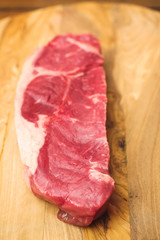 One fresh raw strip loin steak on a wooden cutting board. Meat industry product.