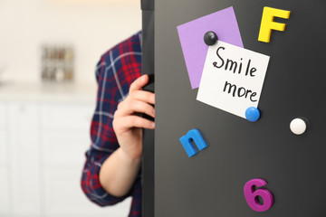 Woman opening refrigerator door with SMILE MORE note indoors, closeup
