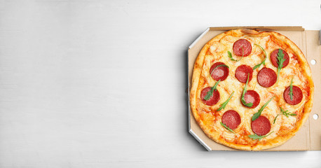 Tasty pepperoni pizza in cardboard box on white wooden table, top view. Space for text