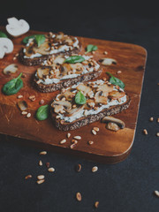 Tasty fresh bruschetta with mushrooms, spinach, garlic, cream cheese and pine nuts, on a wooden board, on a dark background.