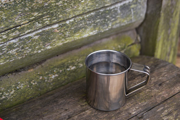 An iron Cup of water on a bench, against the wall of an old wooden house.