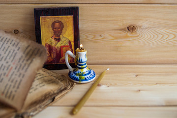 An old Bible, a wooden icon of Saint Nicholas, a wax candle, a Warm tone. Faith.