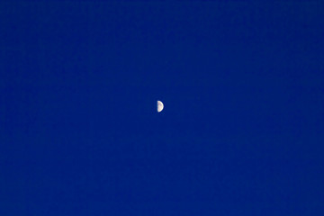 in the dark blue evening sky in the distance half the moon.