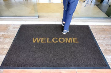 Foto op Plexiglas A welcome mat at the entrance of a cafe restaurant as a customer is seen entering through the front door. © Sweeann