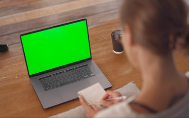 Woman wearing glasses taking notes from laptop Green Mock up Screen