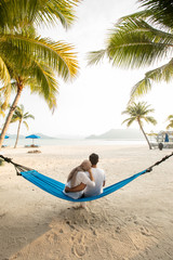 a couple loving hug each other while seating on a hammock at the beach