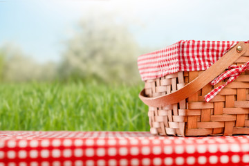 Picnic and summer mood. Picnic basket, on a table with a red tablecloth. Against the background of the landscape. Concept of weekend and summer moods.