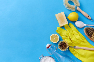 natural cleaning stuff and eco living concept - bottle of vinegar, lemons, rubber gloves, washing soda with soap and brush on blue background