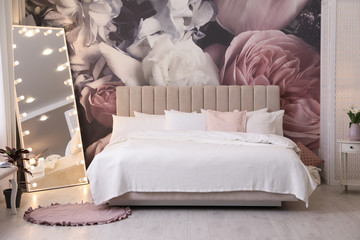 Beautiful room interior with large bed, mirror and floral pattern on wall