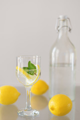 Bottle of cold sparkling mineral water, glass of drink with lemon and mint and whole lemons on glass table. Detox cocktail