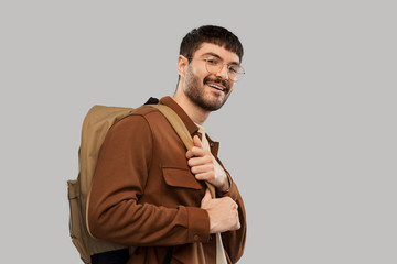 travel, tourism and people concept - smiling young man in glasses with backpack over grey background