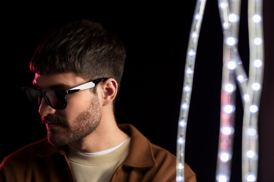 leisure, clubbing and nightlife concept - young man in sunglasses ain dark room over ultra violet neon lights at night club