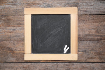 Blackboard with pieces of chalk on wooden background, top view. Space for text