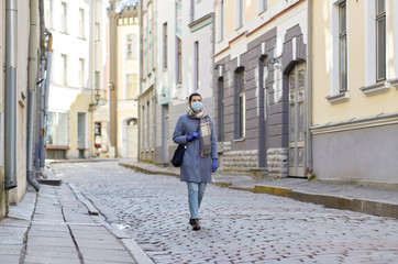 Fototapeta na wymiar health, safety and pandemic concept - young woman wearing protective medical mask on empty street of old town in tallinn city
