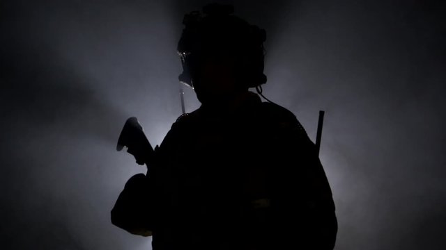 Military soldier in military equipment with a firearm in smoke on a black background. Backlight, military operations, slow mo