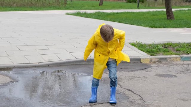 Funny child kid in a yellow raincoat and rubber boots jumping in a puddle