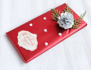 chocolate bar in red wrapping paper decorated with pearls, bump, pine and inscription with the new year