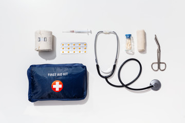 Top view of first aid kit with medical items next to it, isolated on white background.