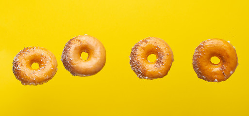 Various decorated donuts in motion falling on a yellow background.