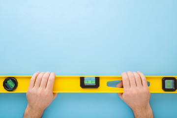 Man hands holding yellow spirit level on light blue table background. Building tool for floor,...