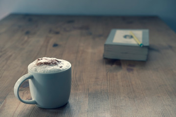 cup with coffee and a closed book on a rustic wooden table