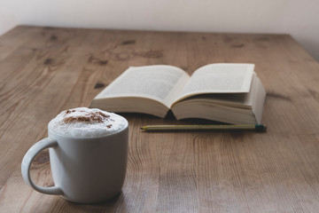 cup with coffee and a open book on a rustic wooden table