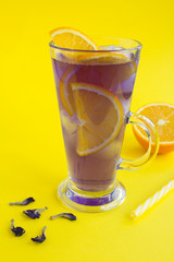 Iced blue flower tea with orange in a glass on the yellow background. Location vertical. Closeup.