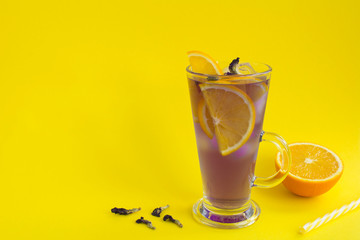 Iced blue flower tea with orange in a glass on the yellow background. Copy space. Closeup.