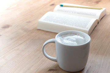 cup with coffee and a open book on a rustic wooden table