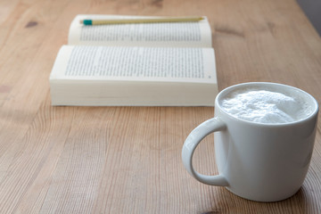 cup with coffee and a open book on a rustic wooden table