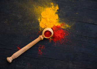 wooden spoon with paprika and scattered yellow and red curry and paprika spices on a black wooden background