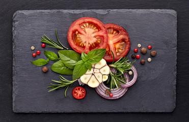 Fresh basil leaves with tomatoes, rosemary and garlic on black stone background. Top view.