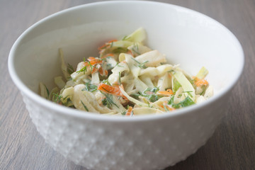 Healthy coleslaw salad with cabbage, carrots, dill and white dressing sauce in a white bowl on wooden surface