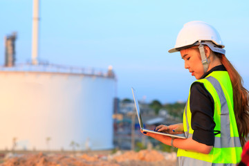 Fototapeta na wymiar Female engineer foreman wearing safety helmet using laptop working in oil refinery industry plant background.