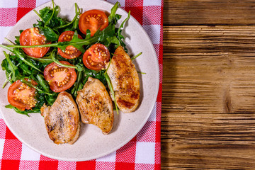 Roasted chicken breasts and salad with arugula and cherry tomatoes in a ceramic plate. Top view