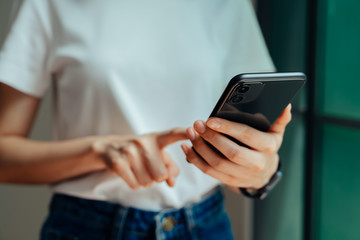Closeup of young woman hand holding smartphone and chatting with friends at social network on the table in cafe.