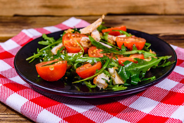 Roasted chicken breasts and salad with arugula and cherry tomatoes in a black plate