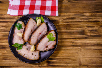 Slices of baked pork belly, garlic and parsley on a black plate. Top view